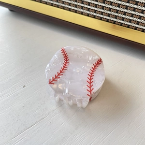 Detail of baseball claw clip with marble texture and red stitching on wooden background