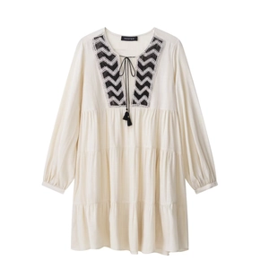 Detail of bohemian cream white dress featuring geometric embroidery and tasseled neck ties
