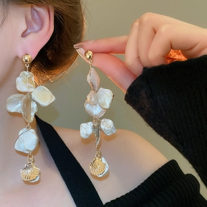 Detail of shell fringe earrings with gold scallop pendants worn on a female model