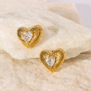 Detailed macro view of 18k gold heart earrings with zircon inlay on a white stone base