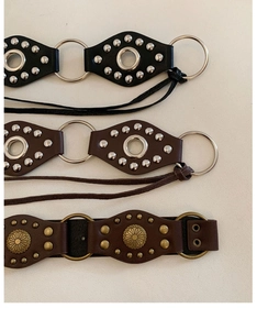 Detail of vintage leather belts with oval cutouts, metal rings, and rivets in brown and black