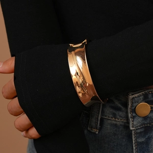 Close-up of wide polished gold metal cuff bracelet with mirror finish on a model's wrist