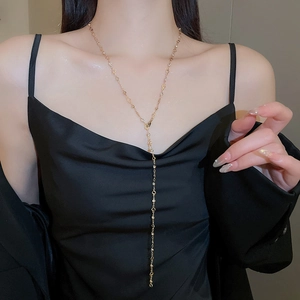 Detail view of a long gold Y-necklace with small metal beads on a model wearing black