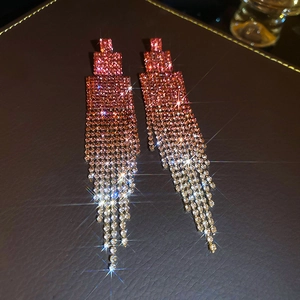Detail of long geometric tassel earrings with pink rhinestones and shiny star flare effect