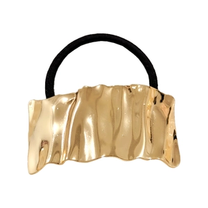 Detailed view of elastic hair tie with wavy gold metal charm and glossy mirror finish