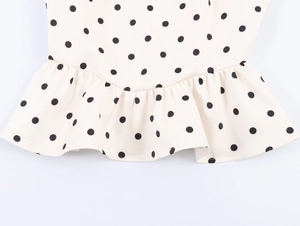 Detail shot of beige polka dot fabric featuring a ruffled hem on the sleeveless top