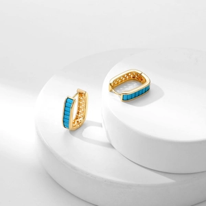Elegant gold zircon hoop earrings with rectangular blue stones on a minimalist stand