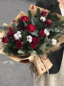 Close-up of bouquet with red roses and pine wrapped in snowflake Kraft paper