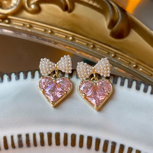 Macro detail of gold-plated bow earrings with pink heart zircon and pearls on white ceramic