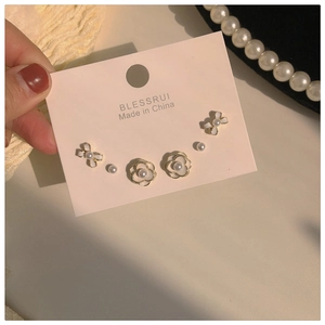 Close-up of pearl camellia and bow stud earrings set on a pink display card