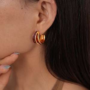 Macro detail of golden double-layered C-shape hoop earrings with dark red enamel inlay