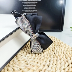 Elegante fermaglio a fiocco nero con strass colorati su un libro e un tappeto di paglia