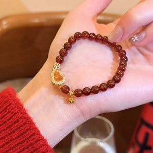 Detailansicht des roten Achat-Perlenarmbands mit einem goldenen Hulu-Anhänger am Handgelenk.