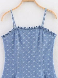 Dettaglio di un abito in denim azzurro con stampa floreale bianca e scollo a volant