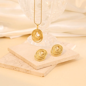 Close-up of golden spiral pendant and earrings set displayed on beige stone plates