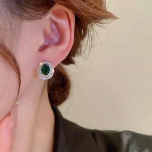 Close-up of emerald zircon stud earring on ear showing elegant oval halo design