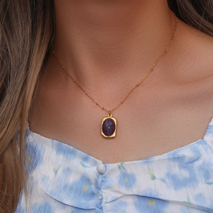 Detail of a vintage oval purple stone pendant on a gold beaded necklace for women