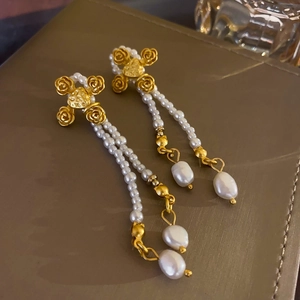 Detail of vintage gold earrings with rose-shaped cross and white baroque pearl tassels