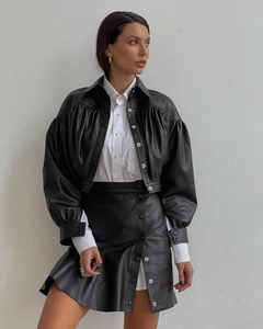 Detailed view of black leather mini skirt with metal buttons and ruffled trim texture