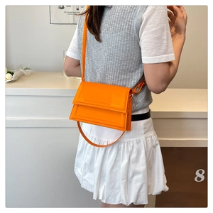 Detail view of bright orange PU leather crossbody bag with flap and dual straps