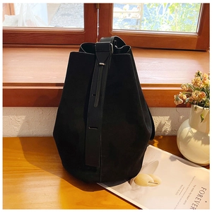 Minimalist black suede bucket tote bag placed on a wooden table with soft natural light