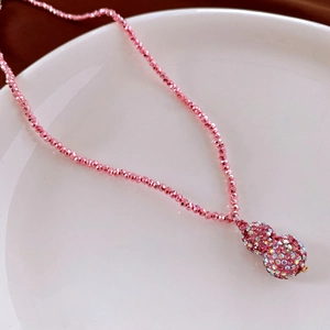 Macro detail of a pink beaded necklace with a crystal-encrusted gourd pendant and tassels