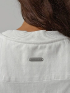 Vue détaillée du col d'un t-shirt blanc en coton avec plaque logo métallique
