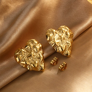 Detail view of heart stud earrings with hammered gold texture on elegant satin fabric