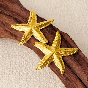 Two golden starfish pendants in 304 stainless steel on a dark textured wood surface