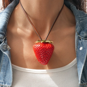Close-up of a large red resin strawberry pendant necklace worn on a leather cord