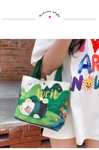 Close-up of canvas tote bag with green forest illustration, cartoon bear and April text