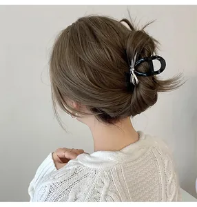 Detail of a black claw clip with a silver metal bow accent worn in a chic bun hairstyle