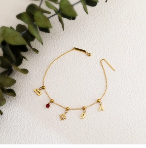 Detail of 18K gold stainless steel charm bracelet with red gem and star pendants