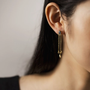 Detail of S925 silver gold earrings with blue pear-shaped stone and long chain tassels