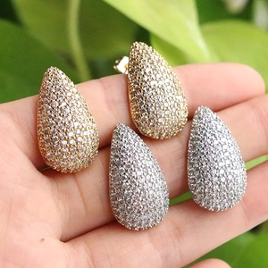 Macro shot of gold and silver teardrop earrings with pavé crystals held against plants