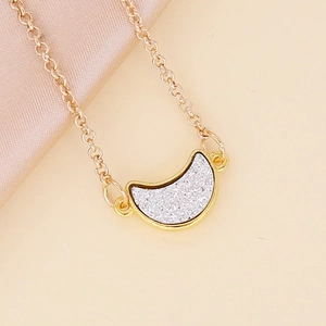 Close-up of gold crescent moon necklace with silver glitter on pink silk background
