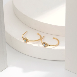 Detail view of gold C-shaped earrings with blue opal evil eye and white zircon stones