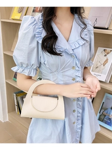 Chic cream small handbag with chain strap shown in a lifestyle setting with bookshelf background