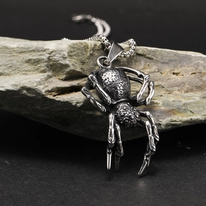 Macro shot of a punk spider pendant in polished silver finish on a dark rock background