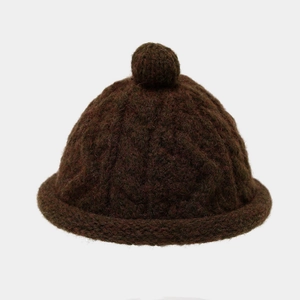 Macro view showing the thick cable knit texture and top pom-pom of the brown beanie