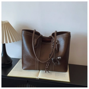 Detail of dark brown tote bag featuring white contrast stitching and cute cat pendant