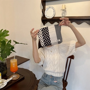 Polka dot and striped fabric pouch held by a model in a cozy cafe setting
