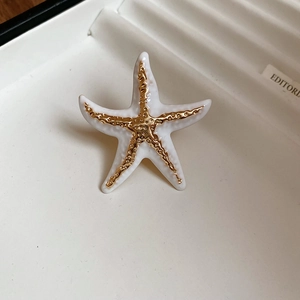 Macro shot of white enamel starfish ring with golden textured center in a gift box