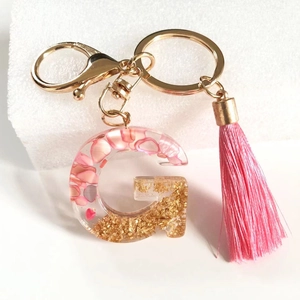 Pink resin initial G keychain with gold foil and tassel on a clean white background