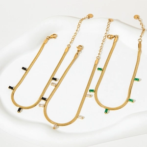 Golden snake chain anklets with colorful zircon gemstones on a white display tray