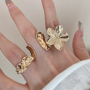 Detail of gold flower ring and irregular hammered open ring worn on a finger