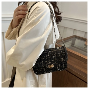 Detail of a black and gold tweed shoulder bag with a metal chain on a cream trench coat