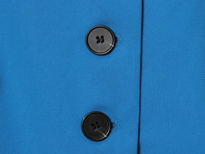 Détail macro du tissu en sergé bleu vif et boutons ronds noirs sur la veste de costume
