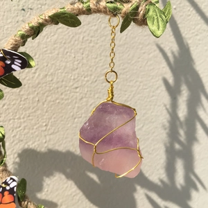 Close-up of raw purple amethyst crystal pendant wrapped in gold wire with green leaves