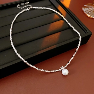 Close-up of crushed silver bead necklace with white pearl pendant on black display tray
